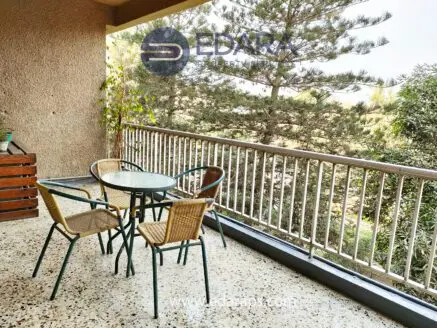 Outdoor balcony with a glass table and four chairs surrounded by greenery.
