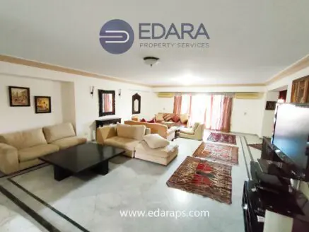 Spacious living room featuring beige sofas, a dark coffee table, and decorative rugs on a marble floor.