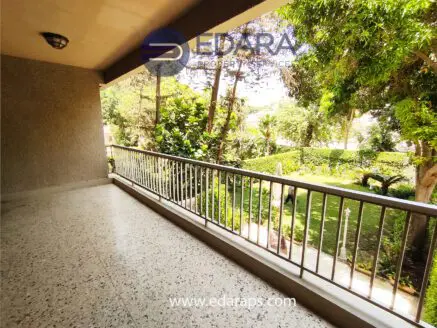 Balcony with a railing overlooking a garden area with trees and greenery.