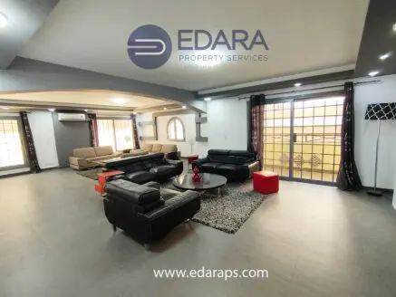 Modern living room featuring black leather sofas, a coffee table, and large windows with natural light.