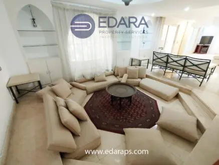 Lounge area featuring a modular beige sofa arranged around a circular coffee table on a patterned rug.