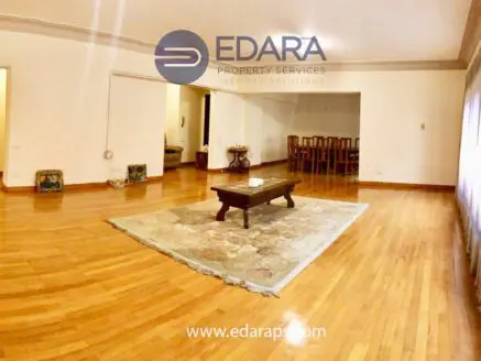 A spacious living room featuring wooden flooring and a central coffee table on a rug.