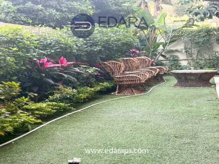 Outdoor seating area featuring rattan chairs and a round table surrounded by greenery.