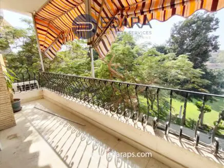 Balcony featuring a wrought iron railing and striped awning, with sunlight casting shadows on the floor.