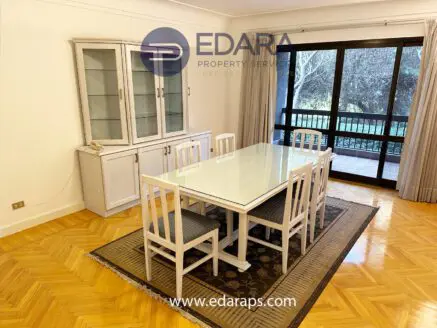 White dining table surrounded by chairs and a display cabinet in a room with wooden flooring.