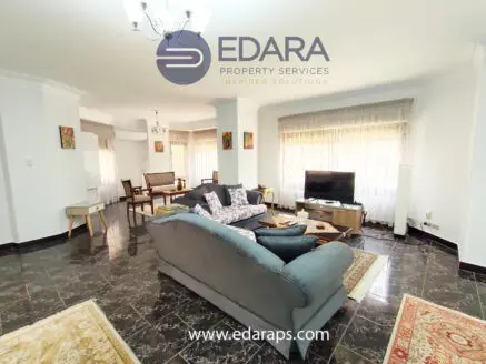 Spacious living room featuring a gray sofa, coffee table, and television with natural light from large windows.
