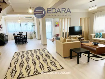 Spacious living room with beige sofa, wooden coffee table, and dining area featuring a table and chairs.