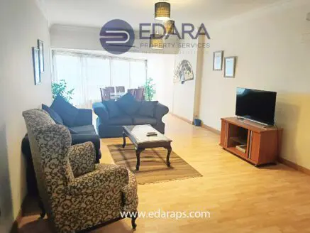 Living room featuring a patterned armchair, sofa, coffee table, and television in a well-lit space.