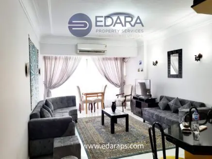 Modern living room featuring gray sofas, a dining area, and a television set against a light-colored wall.