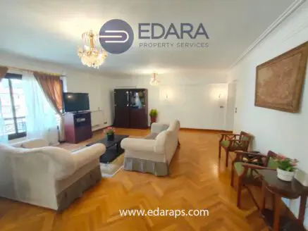 Spacious living room featuring a sofa, chairs, television, and decorative elements in a well-lit environment.