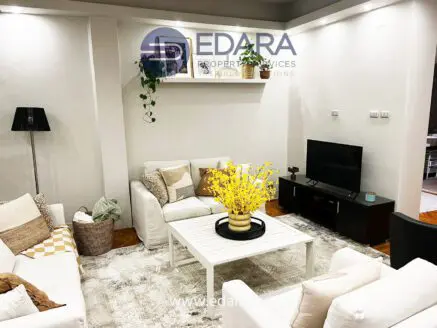 Contemporary living room featuring white sofas, a coffee table, and decorative yellow flowers in a vase.