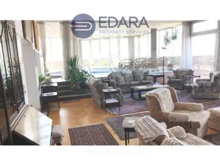 Bright living room featuring floral patterned sofas and large windows allowing natural light.