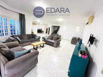 Spacious living room featuring gray sofas arranged around a wooden coffee table on a marble floor.