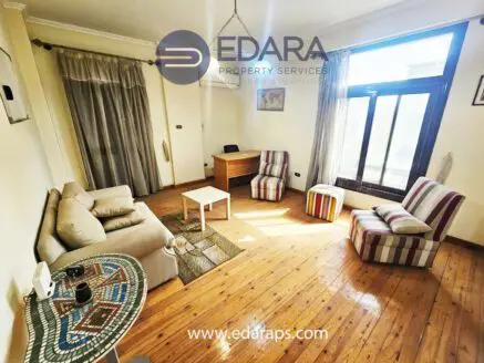 Bright living room featuring a sofa, two striped chairs, and a desk by a large window.