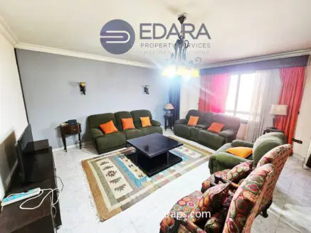 Living room featuring green and multicolored sofas with a coffee table and decorative rug.