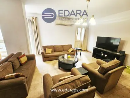 Living room featuring a set of beige sofas arranged around a coffee table and a television on a stand.
