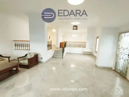 Interior view of a spacious living room featuring marble flooring and a staircase.