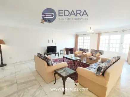 Spacious living room featuring beige sofas, a television, and a coffee table on a marble floor.