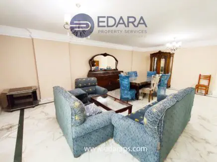 Living room featuring blue upholstered sofas and a wooden dining table with chairs, set in a neutral-toned space.