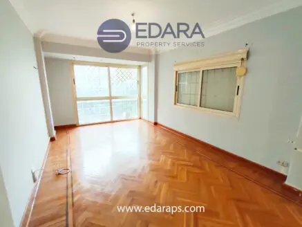 Interior view of an empty room featuring wooden flooring and large windows allowing natural light.