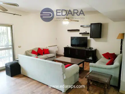 Living room featuring a light-colored sofa set, red cushions, and a television on a dark wooden cabinet.