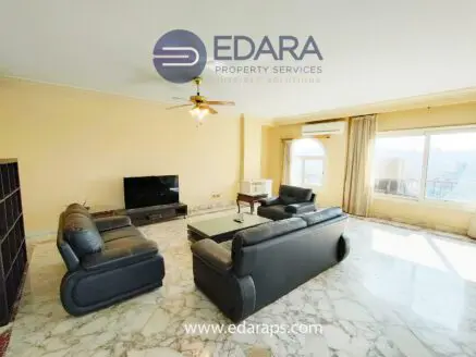 Spacious living room featuring a leather sofa set and marble flooring, with a large window allowing natural light.
