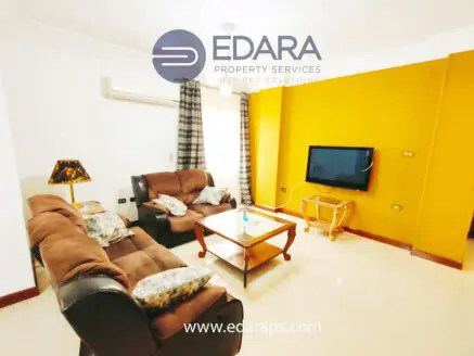 Living room featuring brown leather sofas, a coffee table, and a television against a yellow wall.