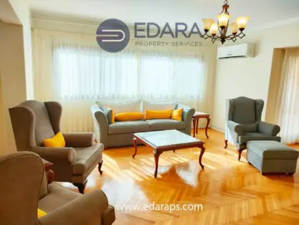 Living room featuring gray upholstered furniture, a wooden coffee table, and large windows with sheer curtains.