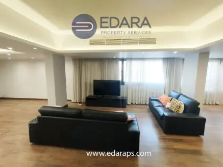Spacious living room featuring two leather sofas and a television against a light backdrop.