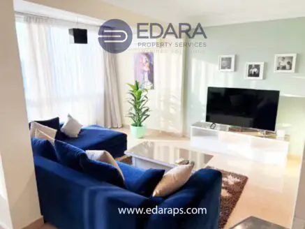 Living room featuring a blue sofa, a television on a white stand, and decorative plants.