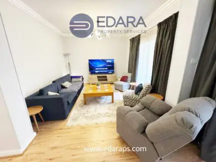 Modern living room featuring a sofa, armchair, and a television mounted on the wall.