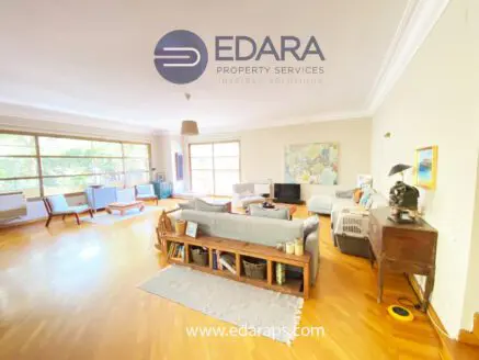 Spacious living room featuring wooden flooring, large windows, and comfortable seating arrangements.
