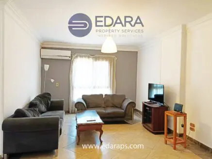 Living room featuring a gray sofa, coffee table, and television set against a light-colored wall.