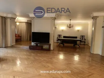 Interior view of a spacious living area featuring wooden flooring and a large television.
