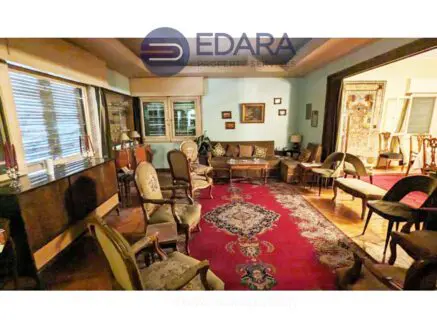 A vintage living room featuring upholstered chairs and a patterned rug in a well-lit space.