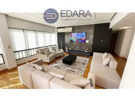 Spacious living room featuring a light-colored sofa set and a flat-screen TV mounted on the wall.