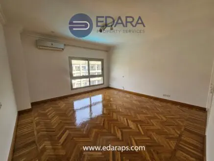 Spacious empty room featuring parquet flooring and large windows allowing natural light.