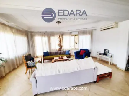 Spacious living room featuring a white sofa, blue and green chairs, and large windows with sheer curtains.