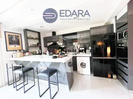 Contemporary kitchen featuring black cabinets, a washing machine, and a breakfast bar with stools.