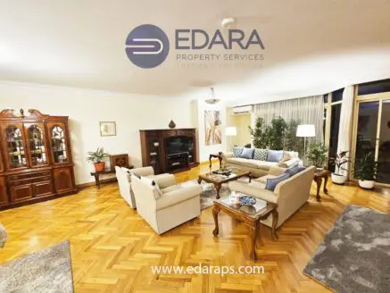 Spacious living room featuring a sofa set, wooden furniture, and decorative elements in a well-lit environment.