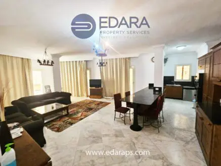 Spacious living room with a dining table and kitchen area in an apartment setting.