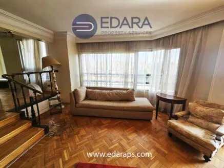 Bright living room featuring a beige sofa, an armchair, and large windows allowing natural light.