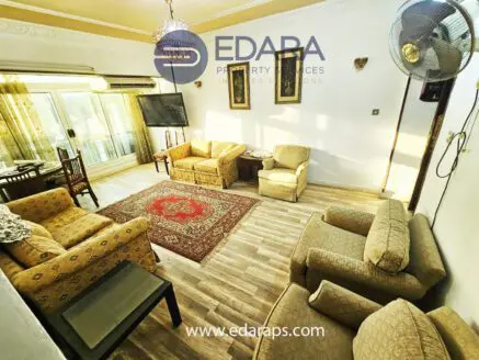 Living room featuring beige upholstered furniture, an area rug, and a television mounted on the wall.