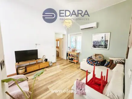 Bright living room featuring a sofa, television, and wooden flooring in a residential setting.