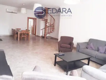 Spacious living room featuring a spiral staircase, seating area, and dining table in a neutral color scheme.