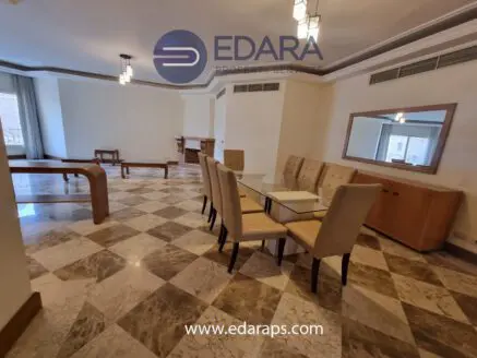 Dining area featuring a glass table surrounded by beige upholstered chairs in a spacious room.