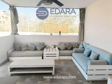 Outdoor seating area featuring a light blue couch, decorative cushions, and a white coffee table.