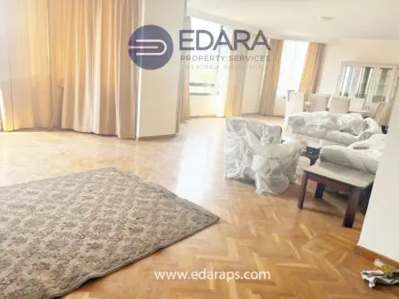Bright living room featuring a large area rug, covered furniture, and large windows with natural light.