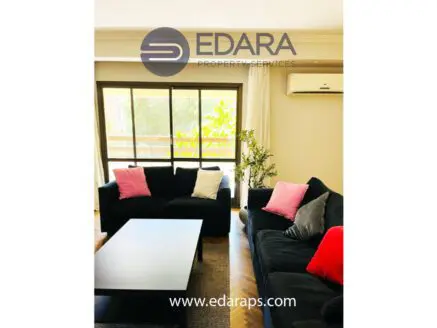Living room featuring black sofas with pink cushions and a coffee table in a well-lit space.