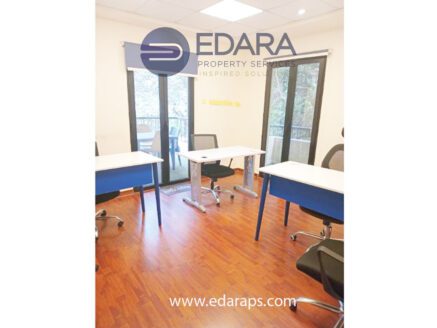 An office workspace featuring two desks and chairs arranged in a bright room with large windows.